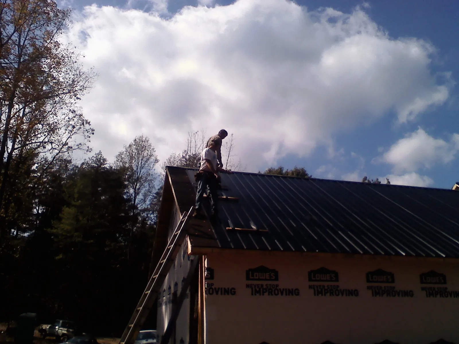 Roofer fastening dark metal panels high against a cloudy sky, from a Roof Inspection job in Weatherford