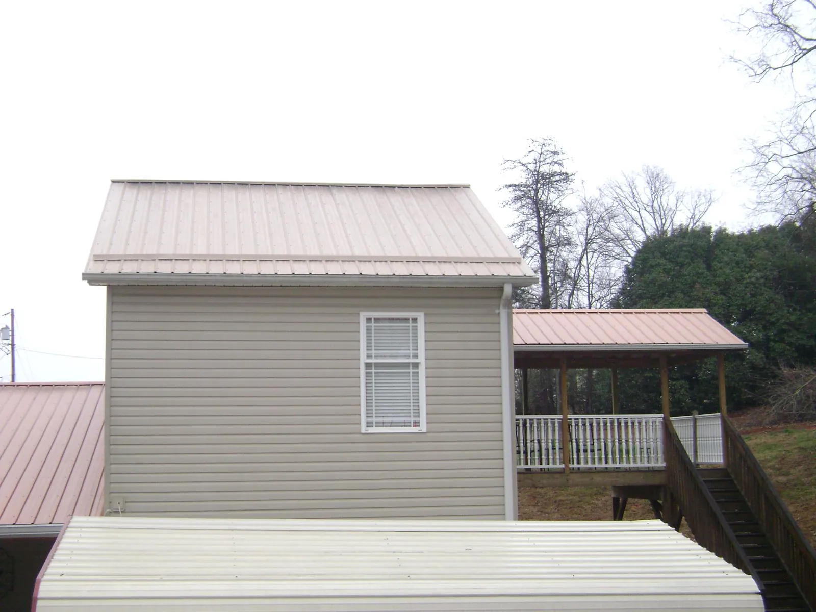 Tan metal roofs on a two story addition and attached porch, from a Roof Replacement job in Weatherford
